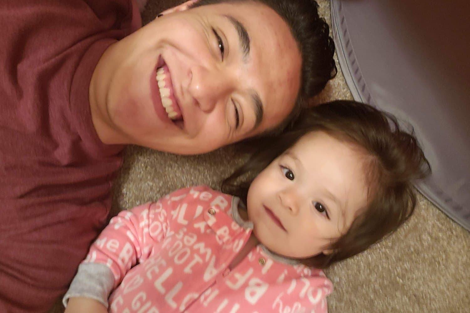 A dad and his toddler lying on the floor, laughing up at the camera